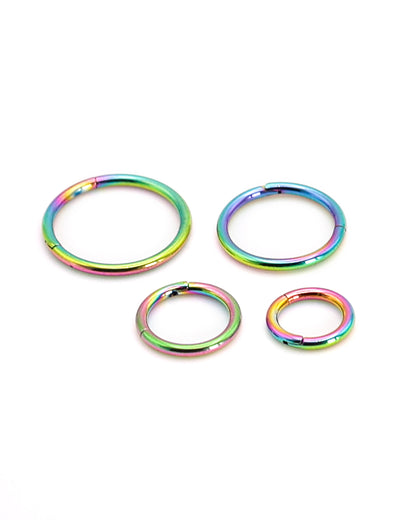 A selection of rainbow coloured titanium clicker hoops on a white background. 
