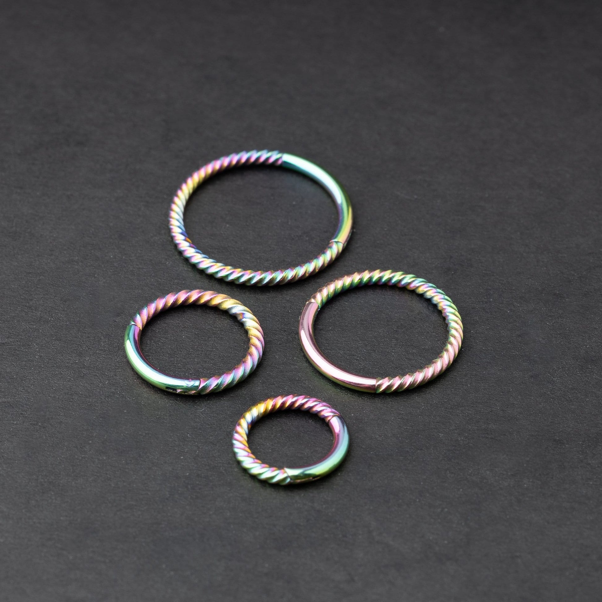 Rainbow twisted clicker rings in varying sizes, displayed on a dark background.