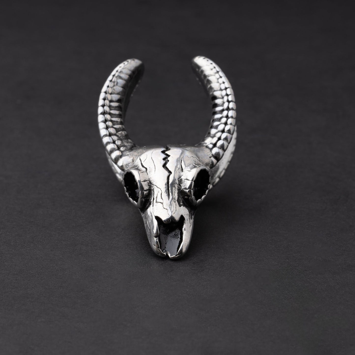 Ram skull saddle tunnel in silver, showcasing intricate skull details and bold design on a dark background.