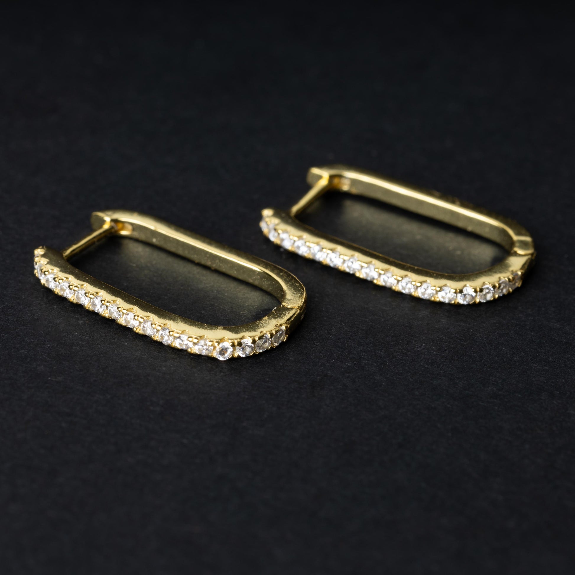 Pair of rectangular gold hoop earrings with crystal embellishments, displayed on a dark background.