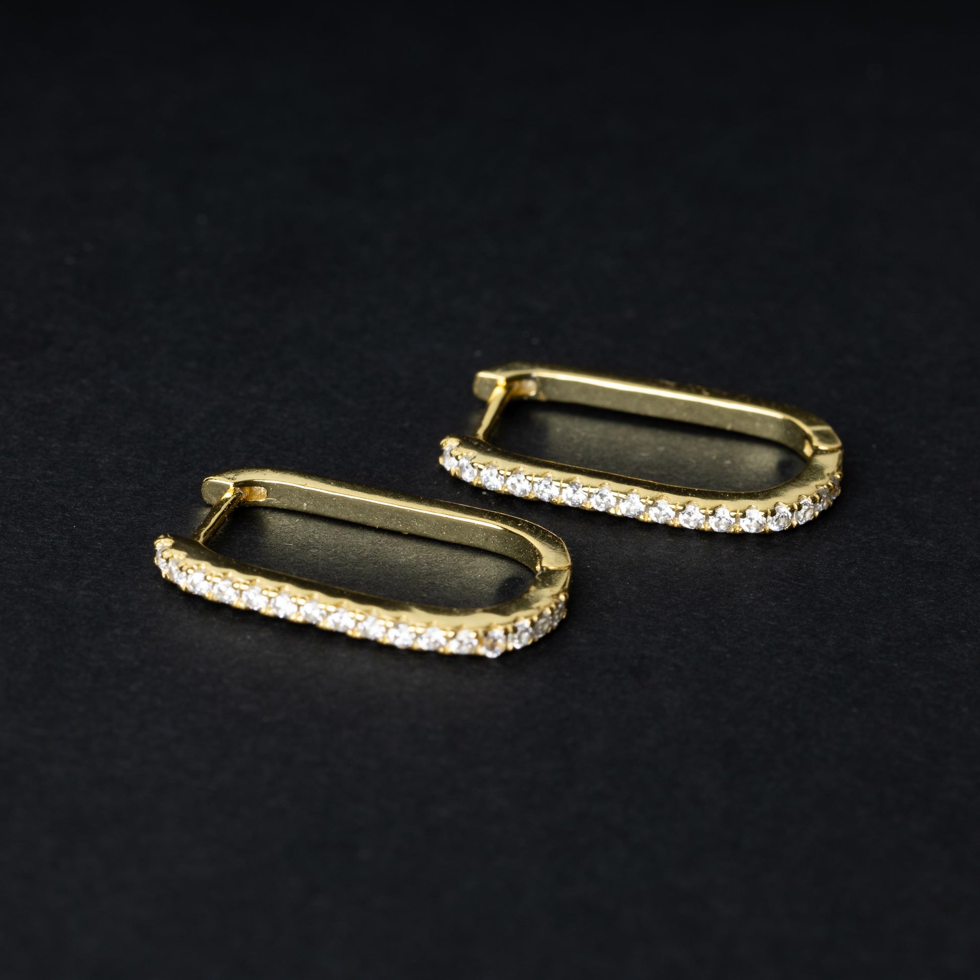 Pair of rectangular gold hoop earrings with crystal embellishments, displayed on a dark background.