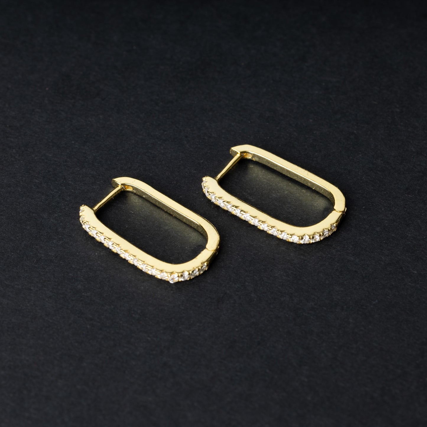 Pair of rectangular gold hoop earrings with crystal embellishments, displayed on a dark background.