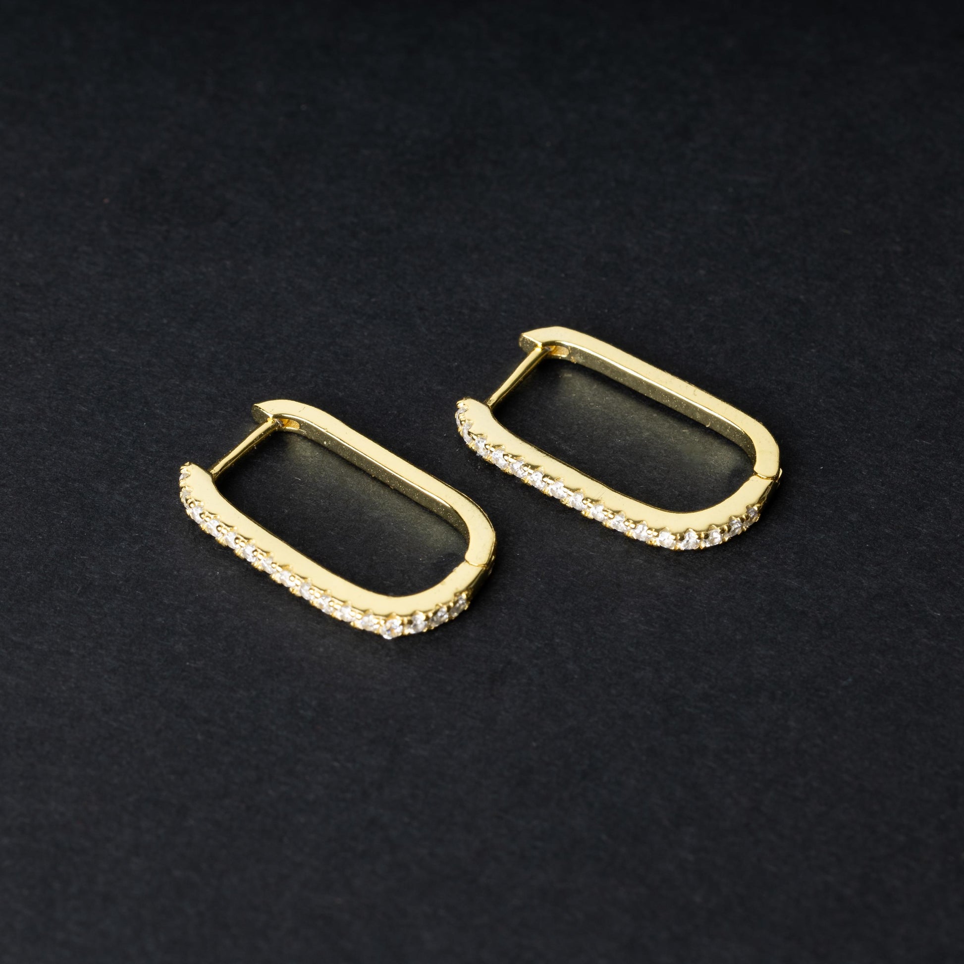 Pair of rectangular gold hoop earrings with crystal embellishments, displayed on a dark background.