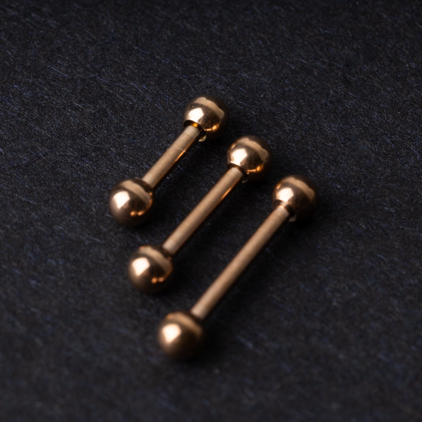 Rose Gold-tone stainless steel barbells on a dark background.