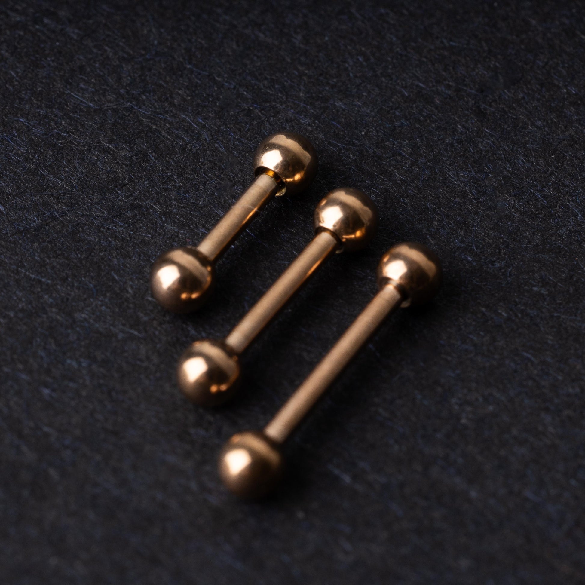 Rose Gold-tone stainless steel barbells on a dark background.