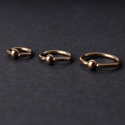 Rose Gold-tone ball closure rings in three sizes, displayed on a dark background.
