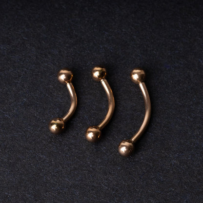 Three rose gold-tone stainless steel curved barbells of varying sizes displayed on a dark background.