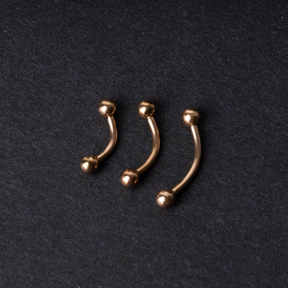 Three rose gold-tone stainless steel curved barbells of varying sizes displayed on a dark background.
