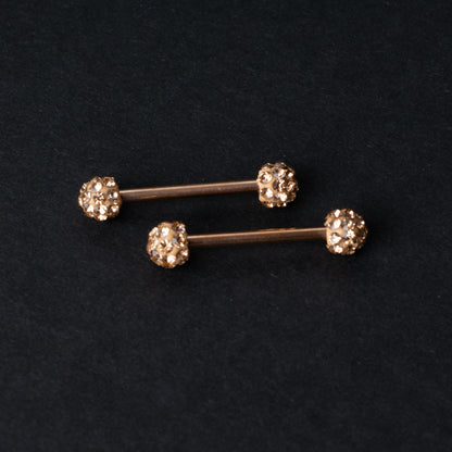 Barbells with textured crystal-encrusted ends in rose gold displayed on a dark background.