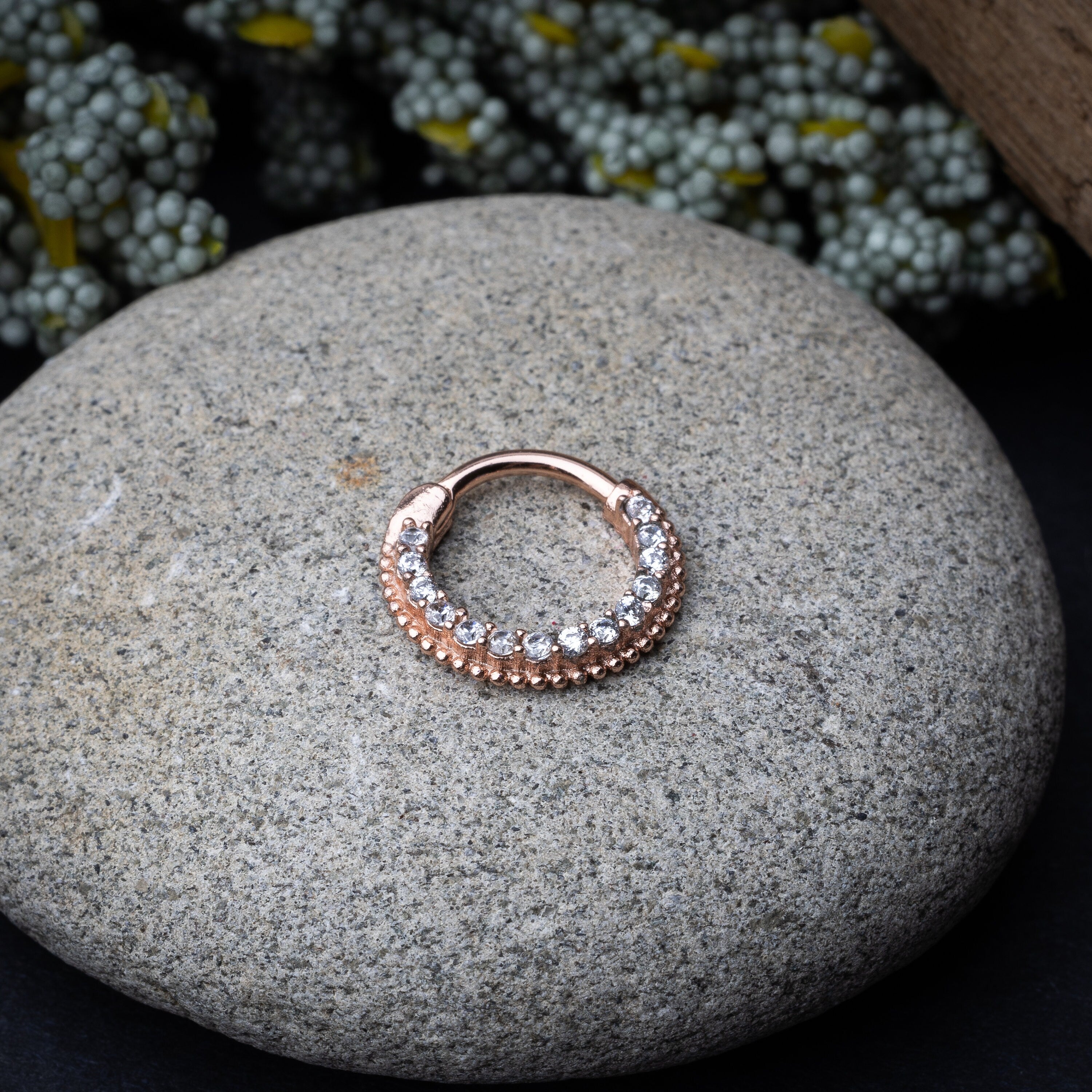 Stainless steel clicker with double rows of clear gemstones in rose gold displayed on a stone background