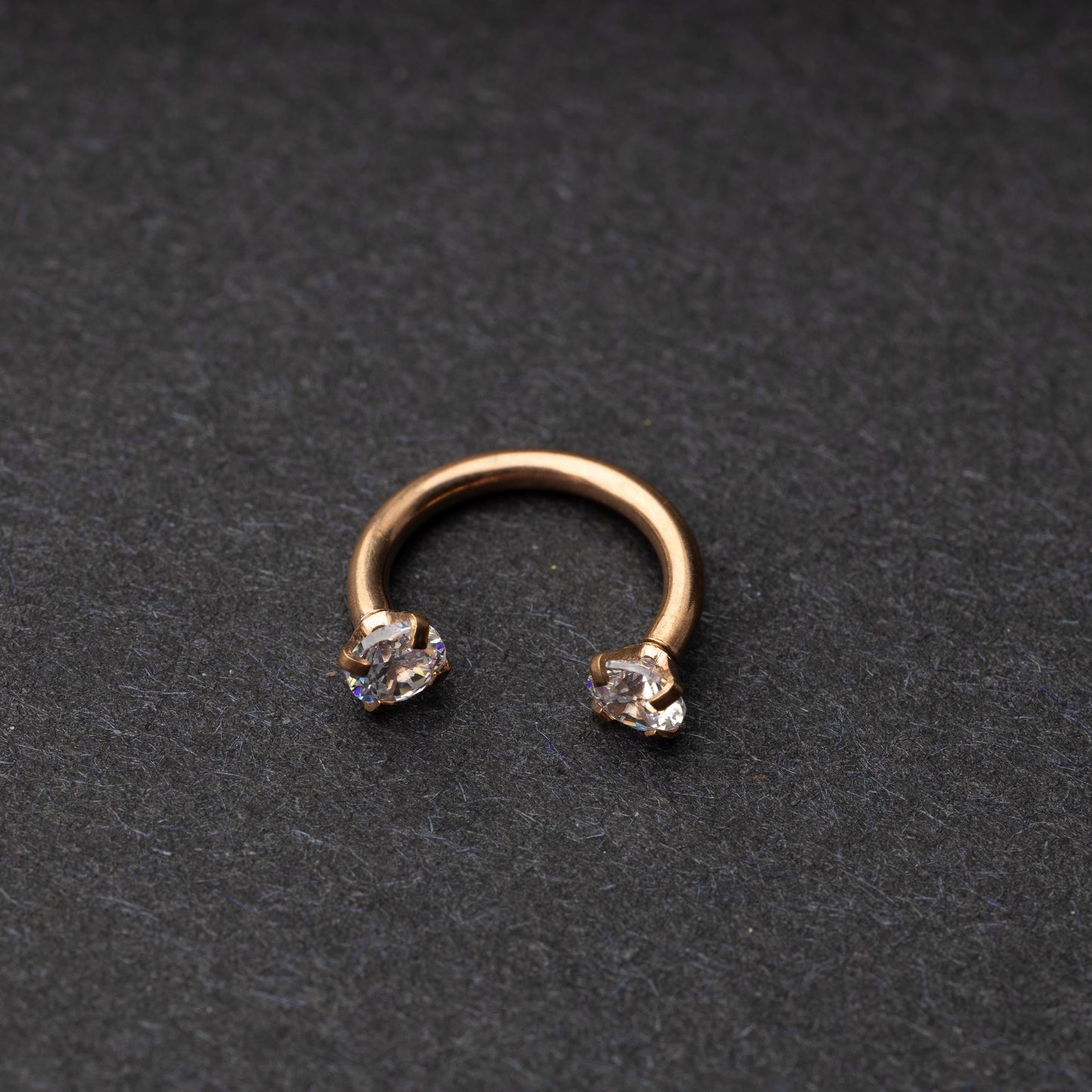A rose gold jewelled horseshoe hoop with gemstone ends, displayed on a dark background.