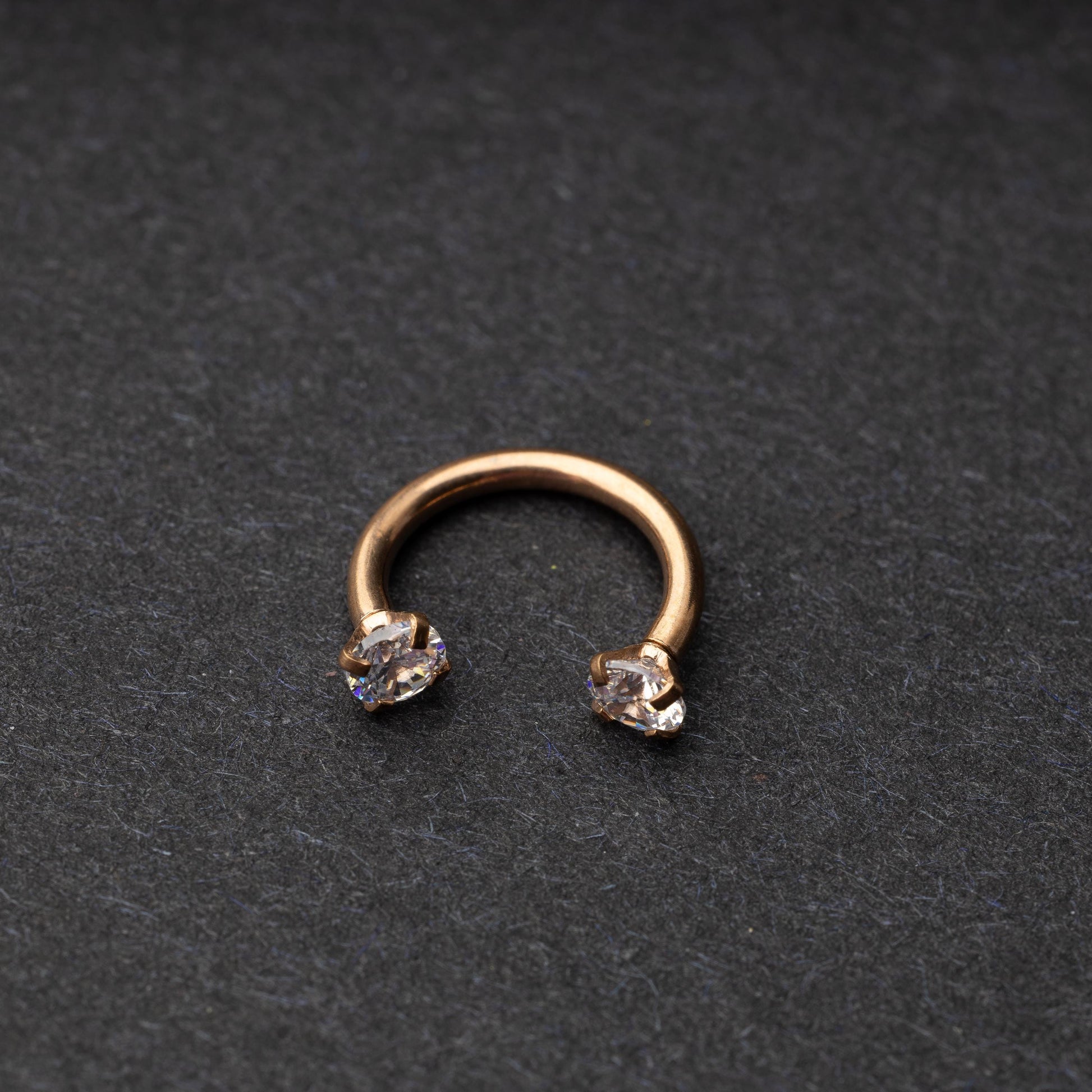 A rose gold jewelled horseshoe hoop with gemstone ends, displayed on a dark background.