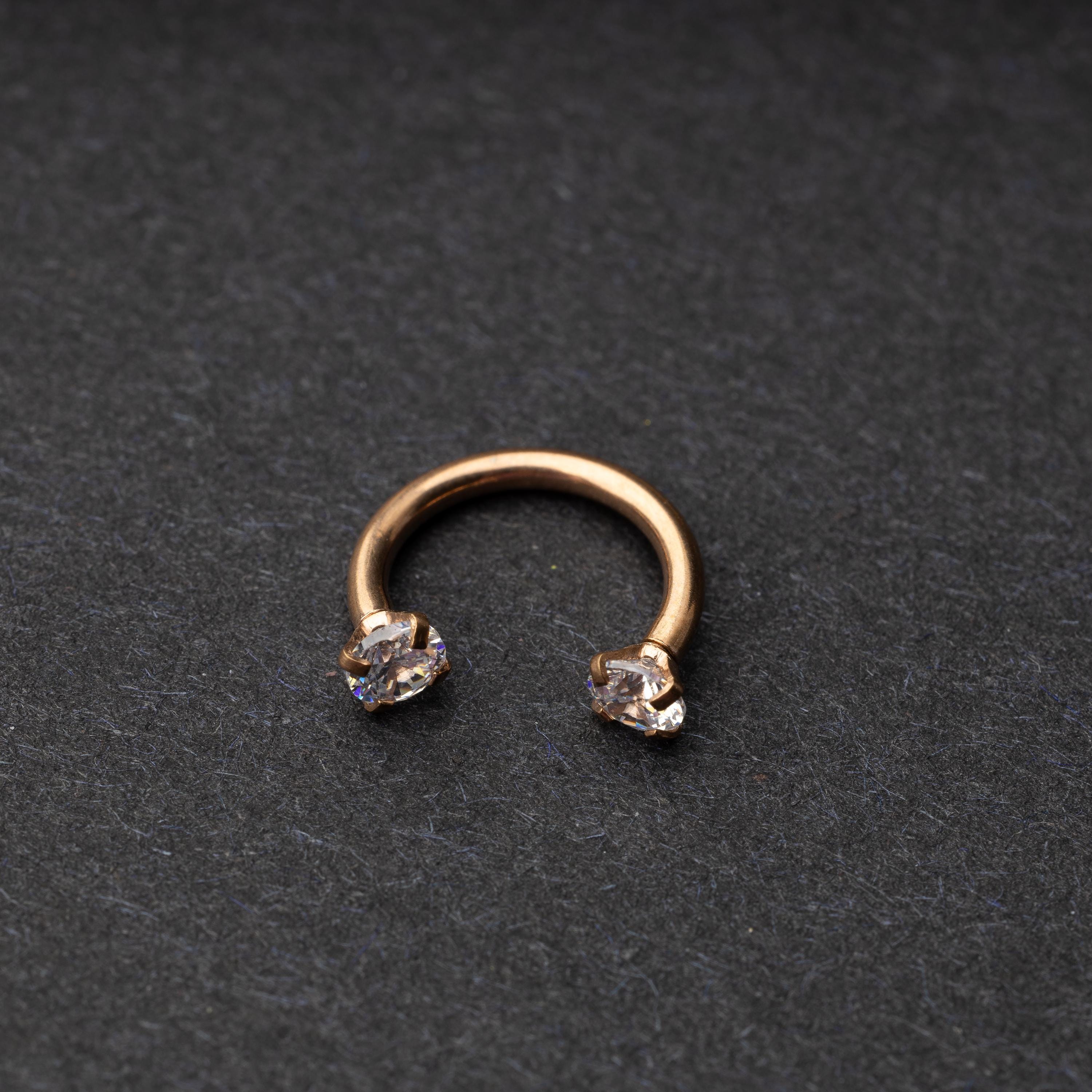 A rose gold jewelled horseshoe hoop with gemstone ends, displayed on a dark background.