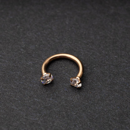 A rose gold jewelled horseshoe hoop with gemstone ends, displayed on a dark background.