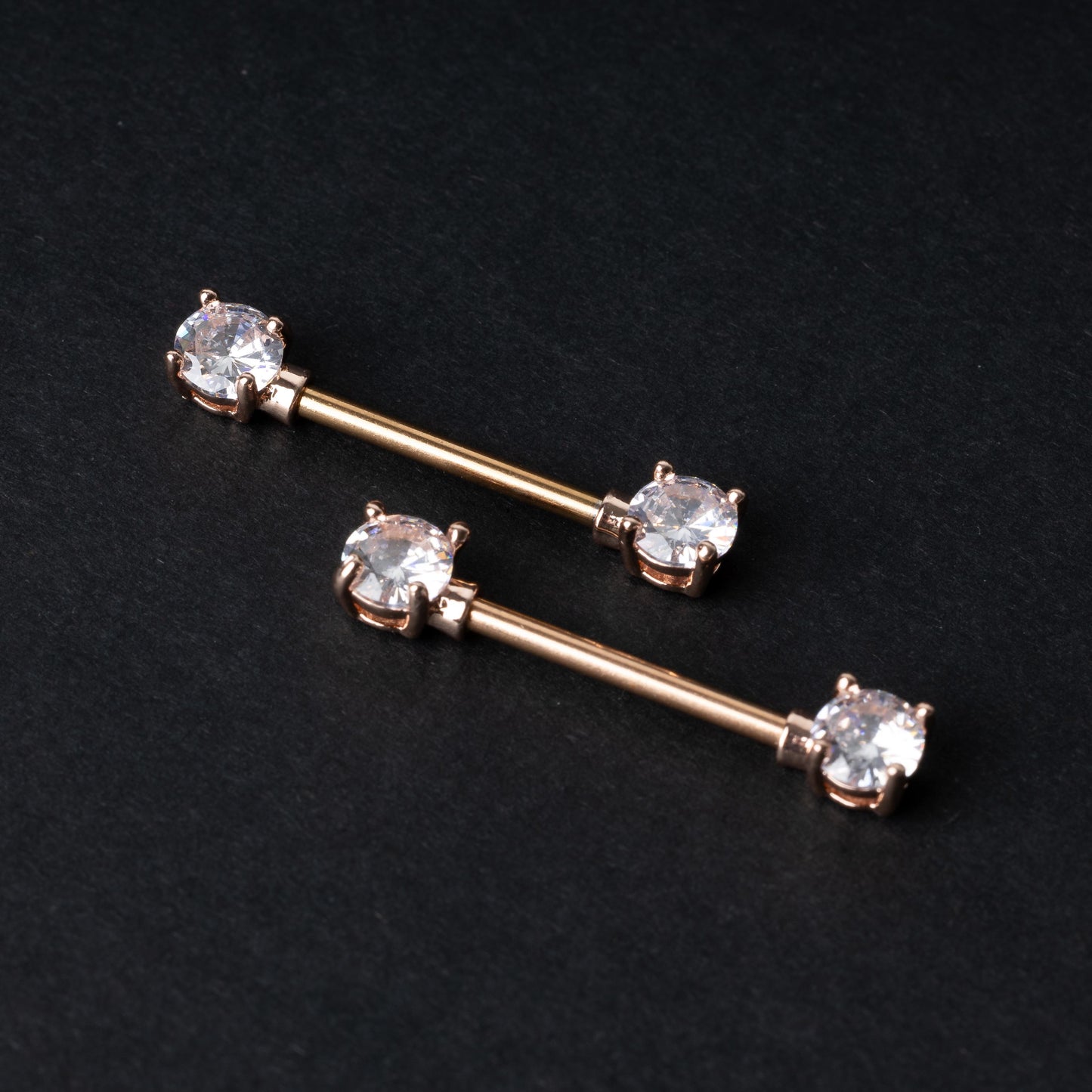 Two Crystal-studded barbells in rose gold displayed on a dark background.