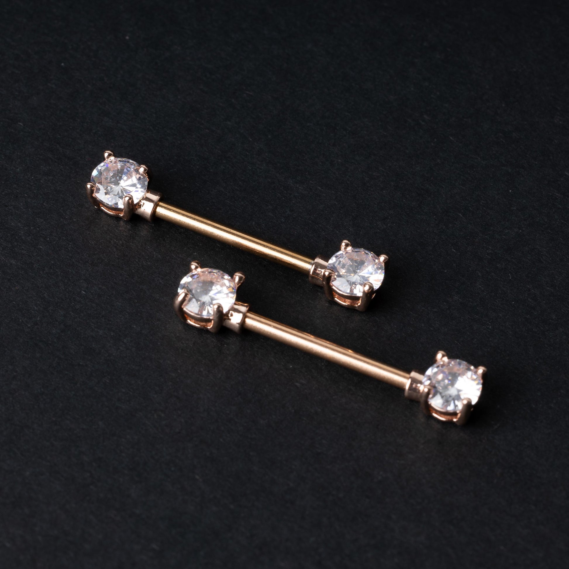 Two Crystal-studded barbells in rose gold displayed on a dark background.