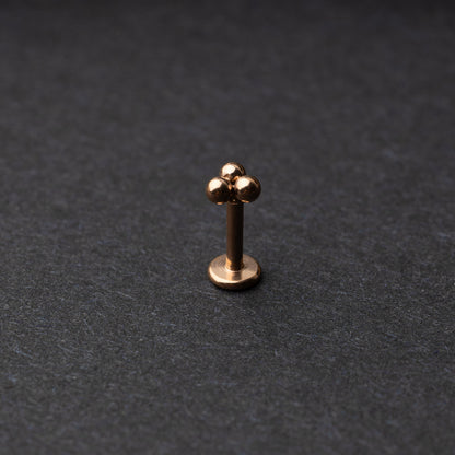Close-up of three minimalist ball cluster labret studs in a rose gold finish, displayed on a dark background.
