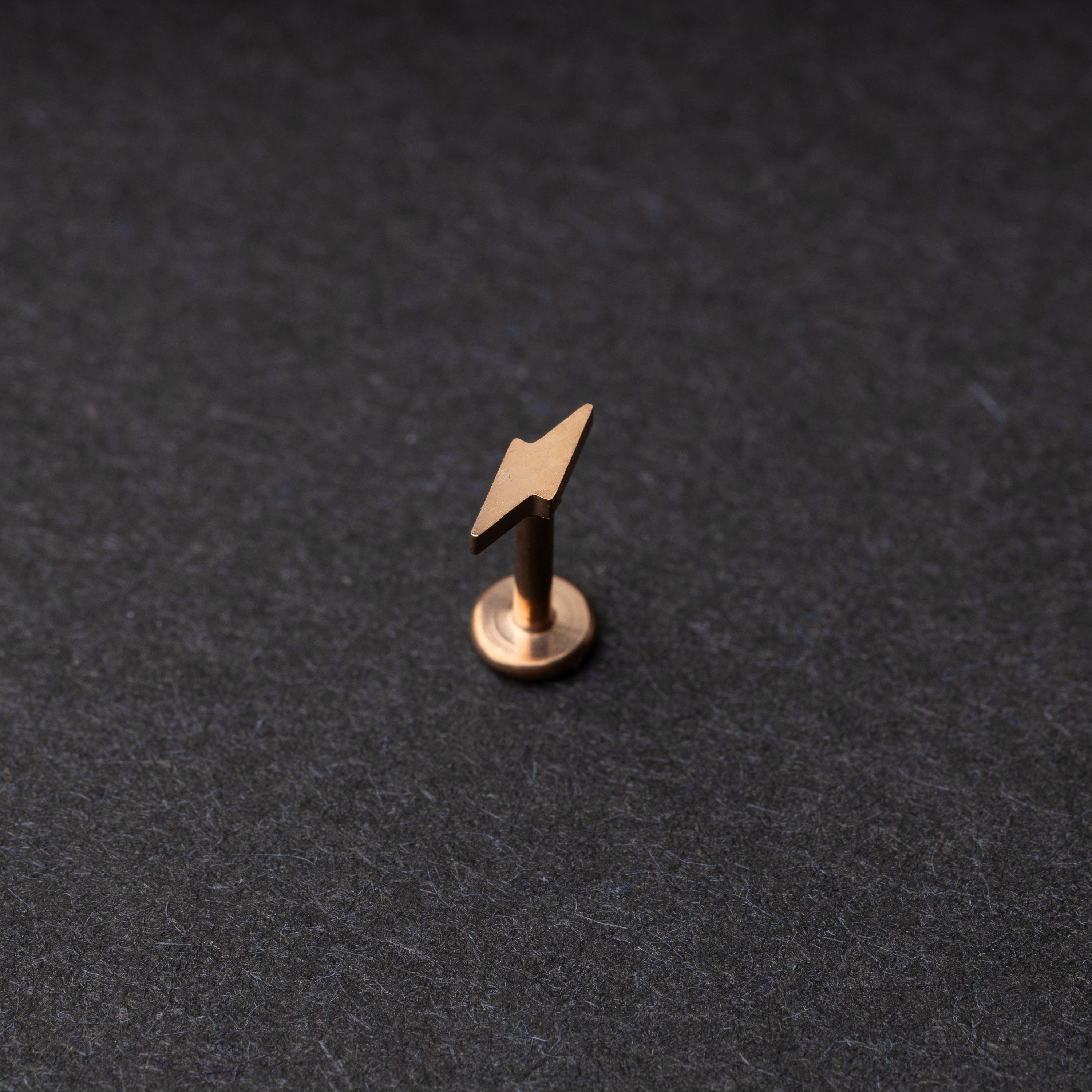 Minimalist lightning bolt labret studs in rose gold displayed on a dark background.