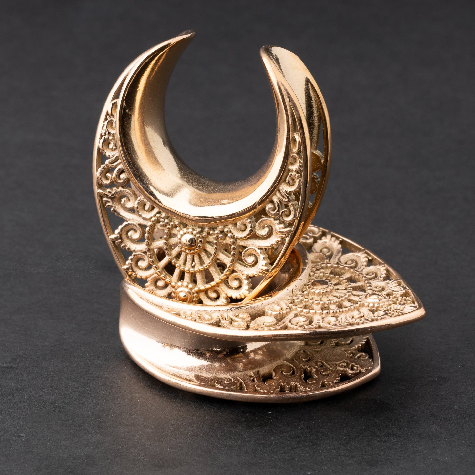 Crescent moon plugs for stretched ears in rose gold, displayed against a dark background.