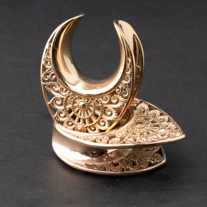 Crescent moon plugs for stretched ears in rose gold, displayed against a dark background.