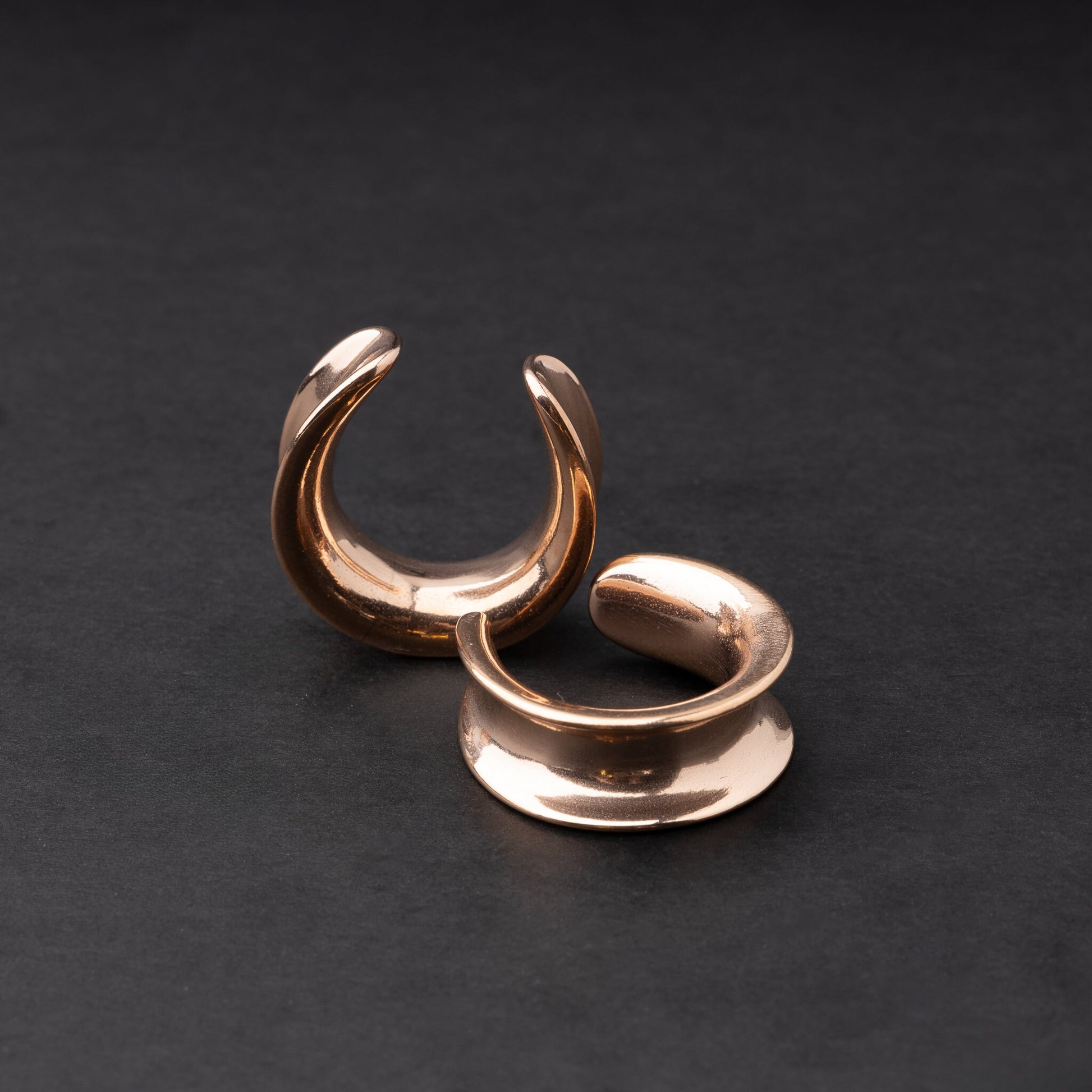A pair of rose gold saddle tunnels displayed on a dark background.