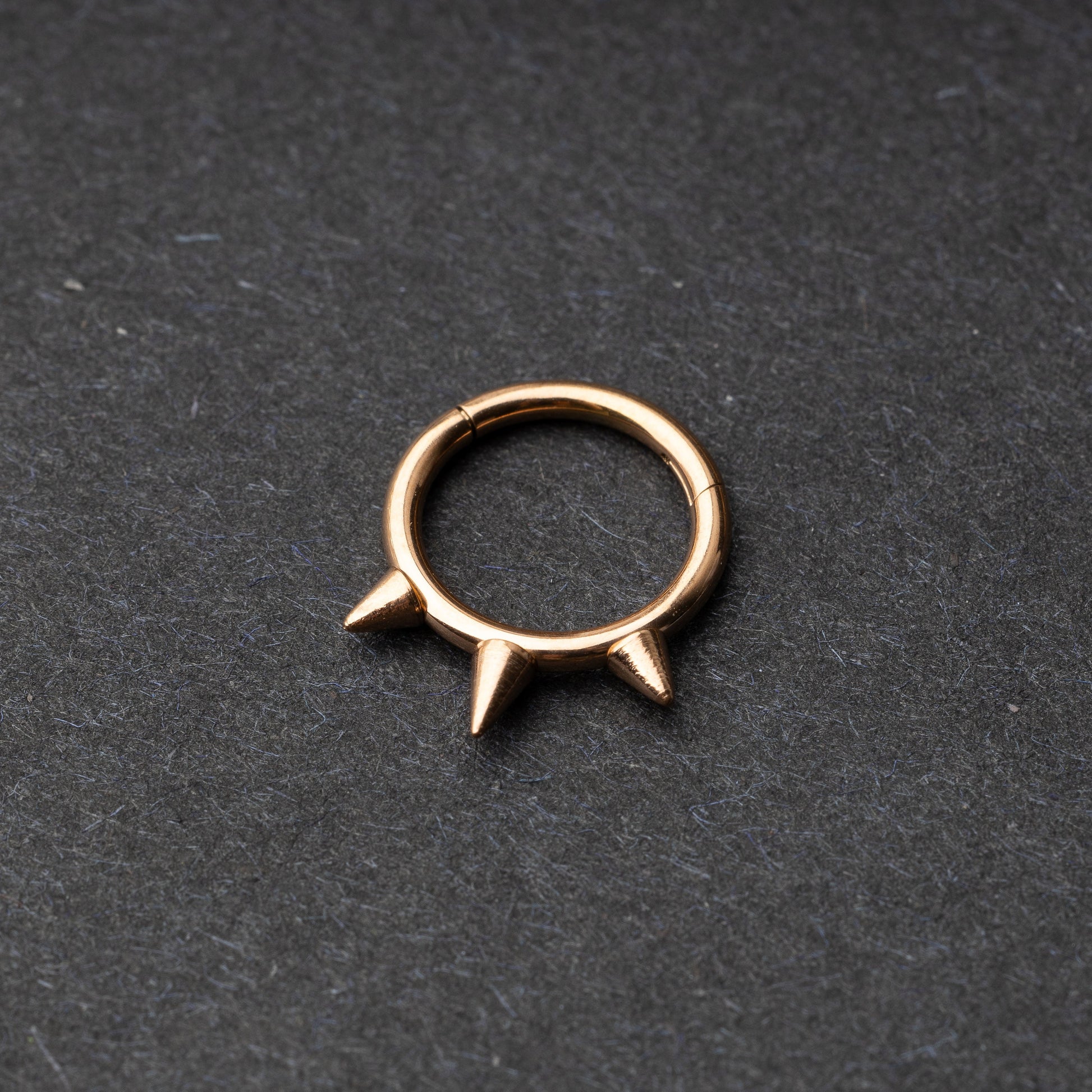 Rose Gold-tone stainless steel clicker ring with three spikes, displayed on a dark textured background.
