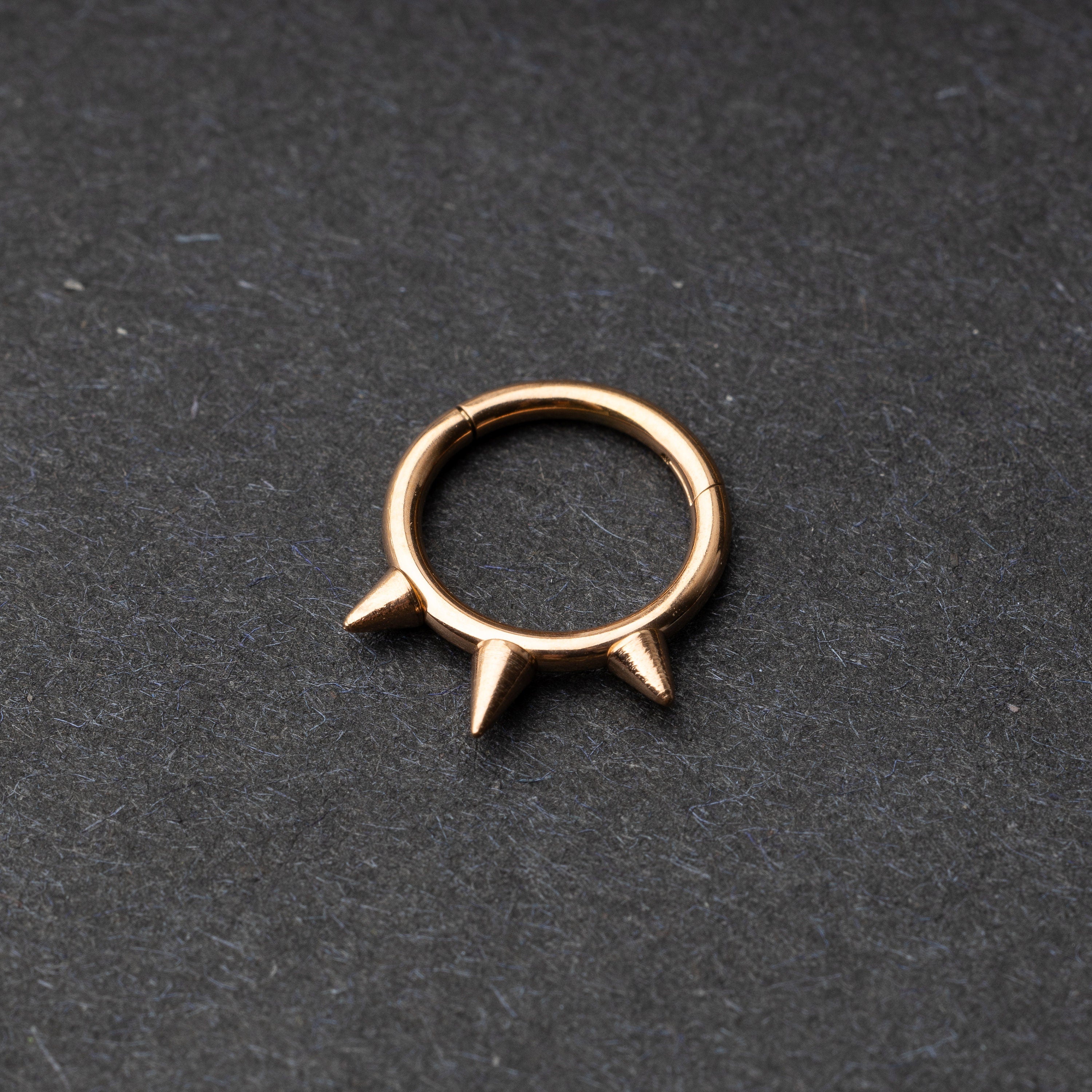 Rose Gold-tone stainless steel clicker ring with three spikes, displayed on a dark textured background.