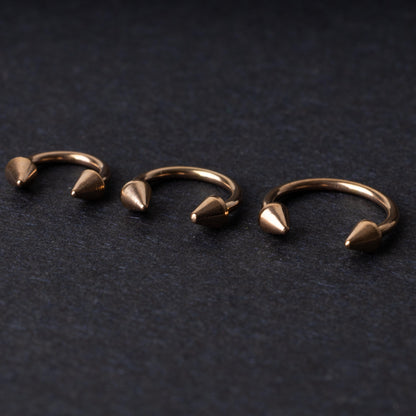 Three rose gold-tone horseshoe hoops with threaded spike ends arranged on a dark textured background.