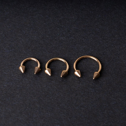 Three rose gold-tone horseshoe hoops with threaded spike ends arranged on a dark textured background.