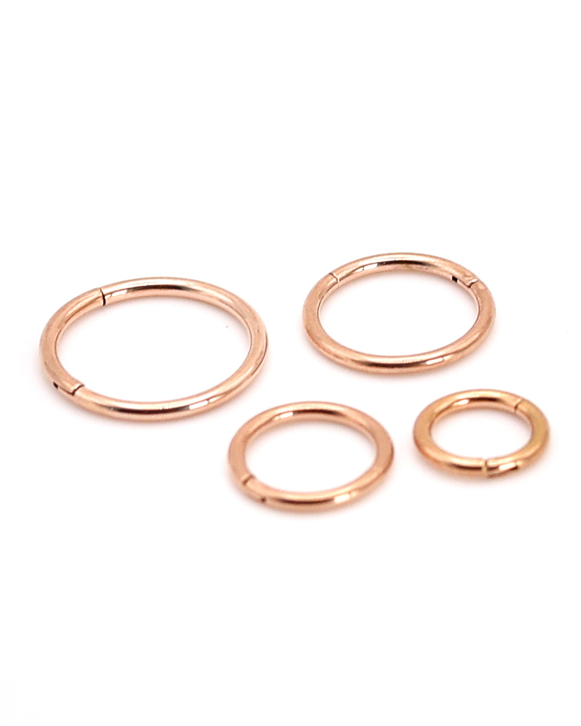 A selection of rose gold coloured titanium clicker hoops on a white background. 
