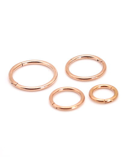 A selection of rose gold coloured titanium clicker hoops on a white background. 

