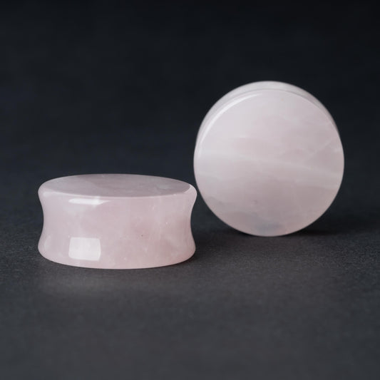 Two polished double-flared stone plugs with a soft, natural color and smooth surface, displayed on a dark background.

