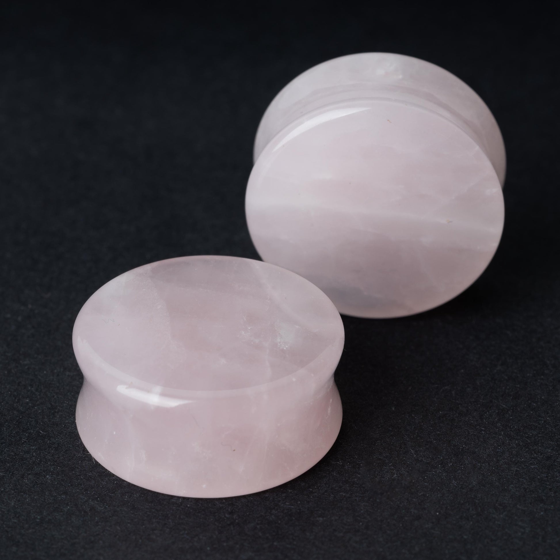  Two polished double-flared stone plugs with a soft, natural color and smooth surface, displayed on a dark background.

