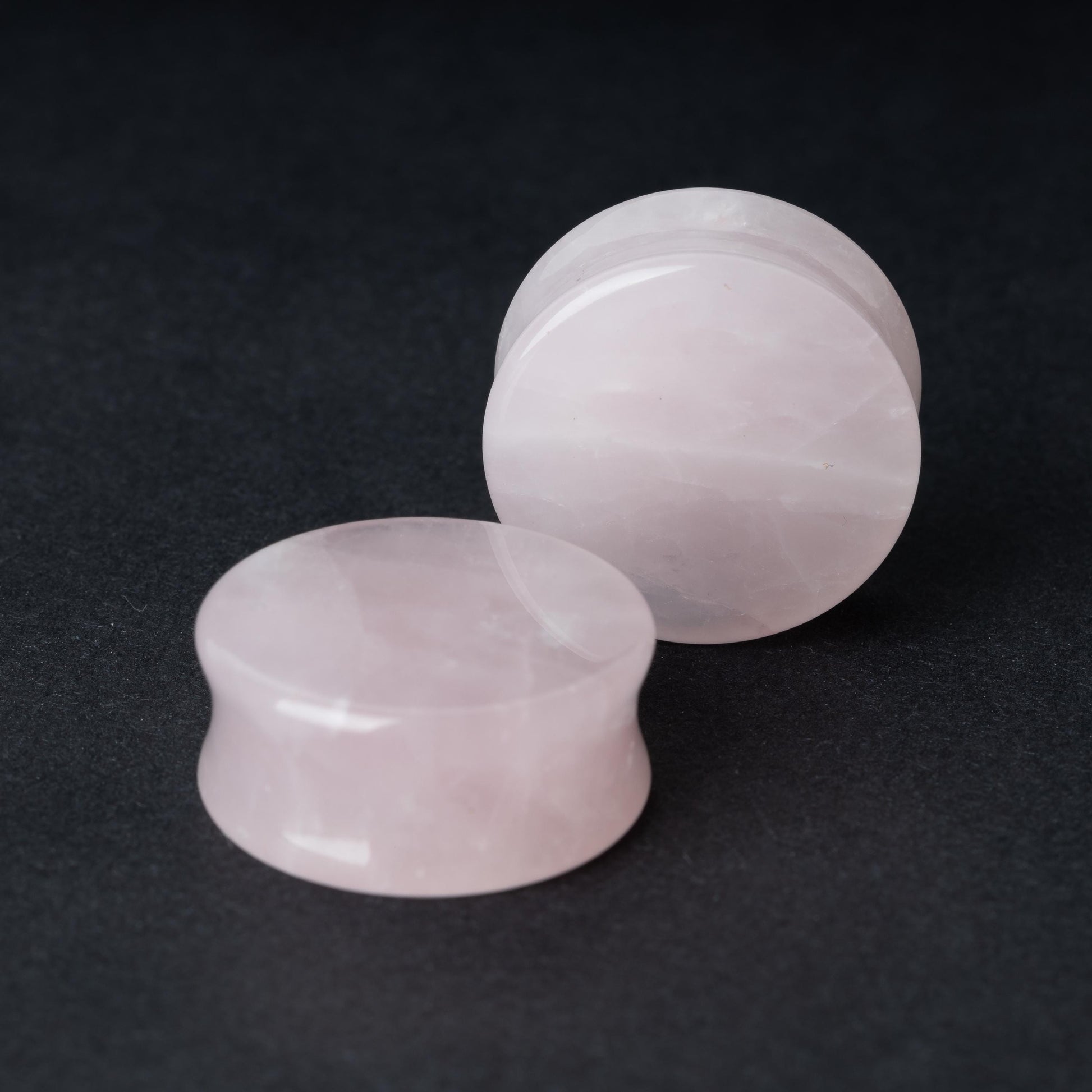 Two polished double-flared stone plugs with a soft, natural color and smooth surface, displayed on a dark background.

