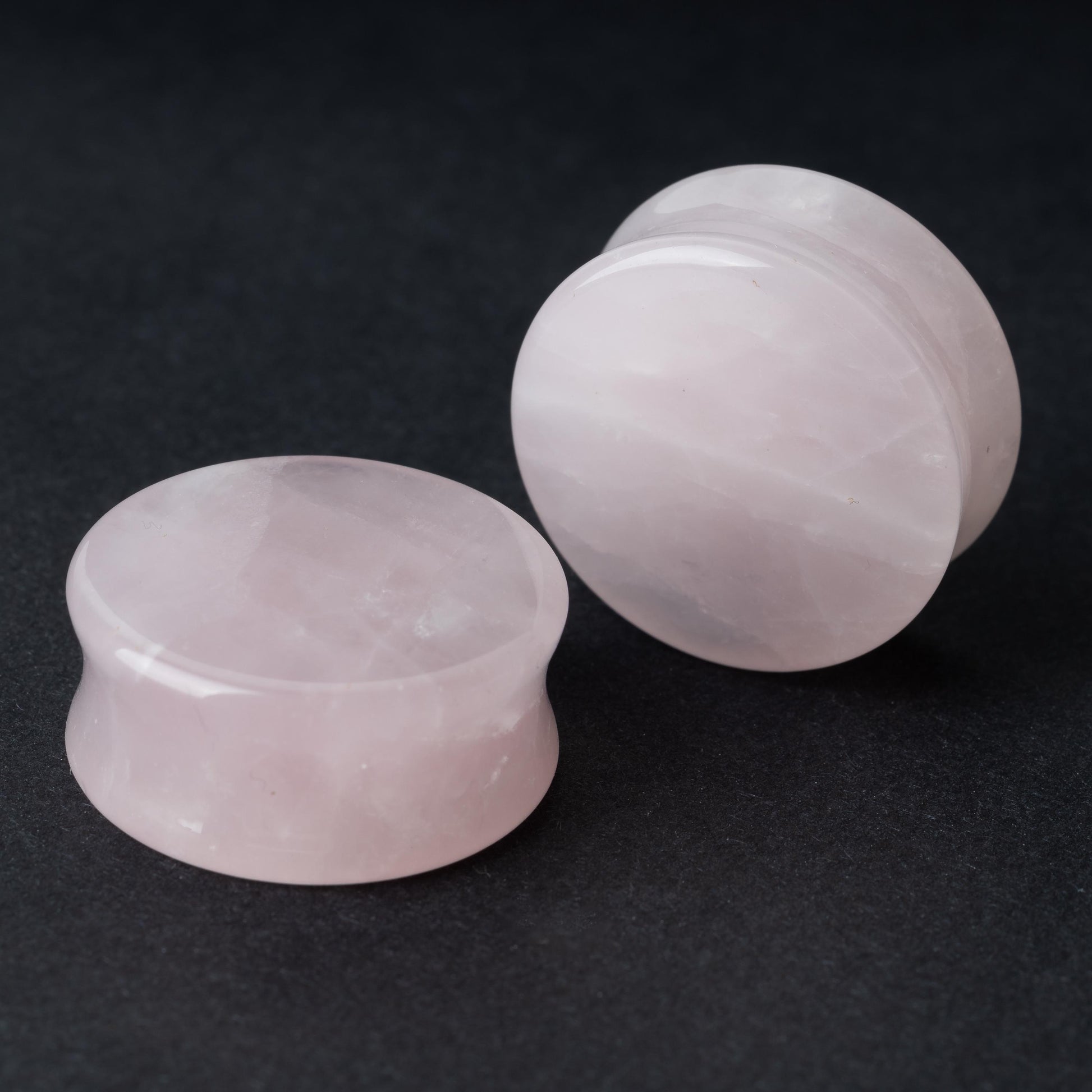 Two polished double-flared stone plugs with a soft, natural color and smooth surface, displayed on a dark background.

