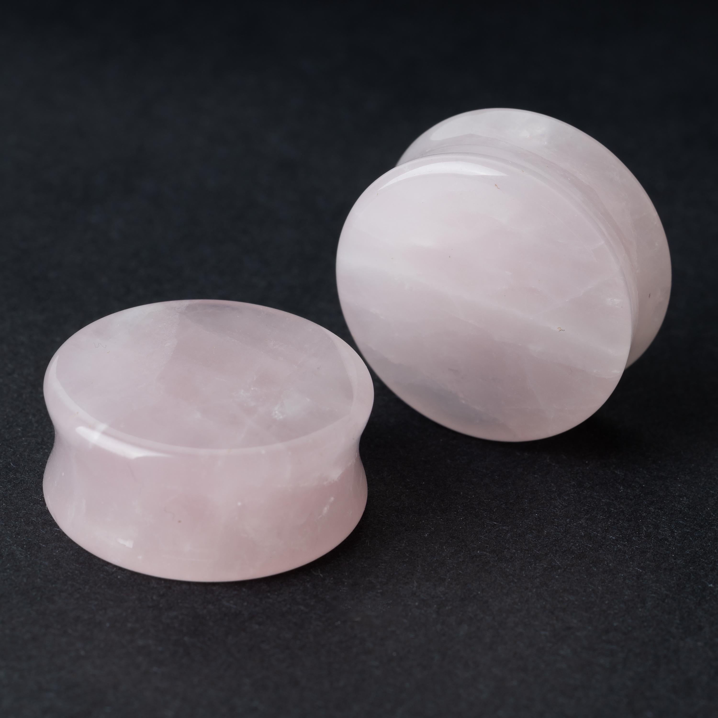 Two polished double-flared stone plugs with a soft, natural color and smooth surface, displayed on a dark background.

