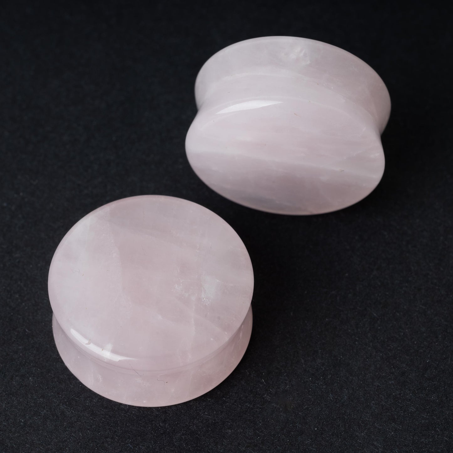 Two polished double-flared stone plugs with a soft, natural color and smooth surface, displayed on a dark background.

