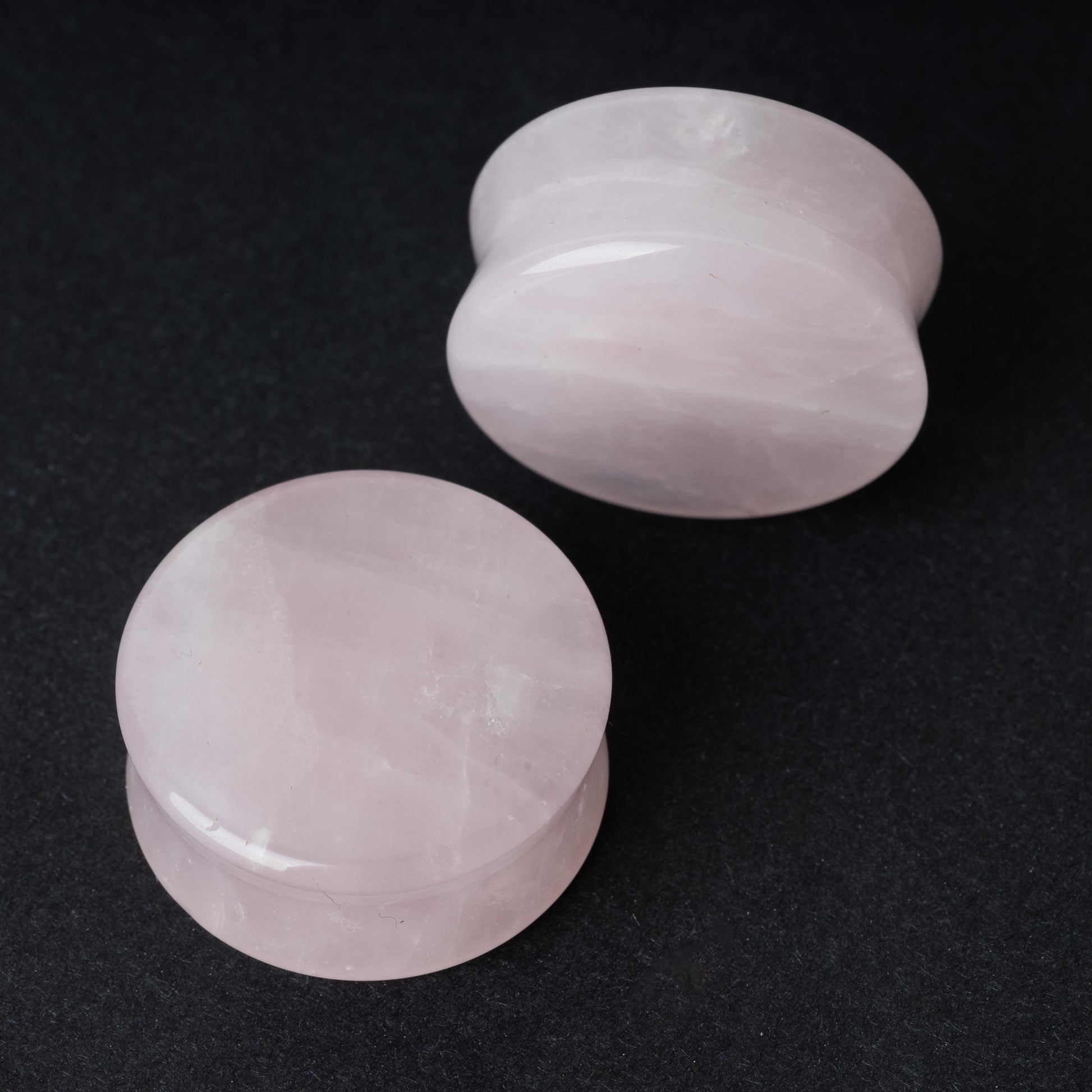 Two polished double-flared stone plugs with a soft, natural color and smooth surface, displayed on a dark background.

