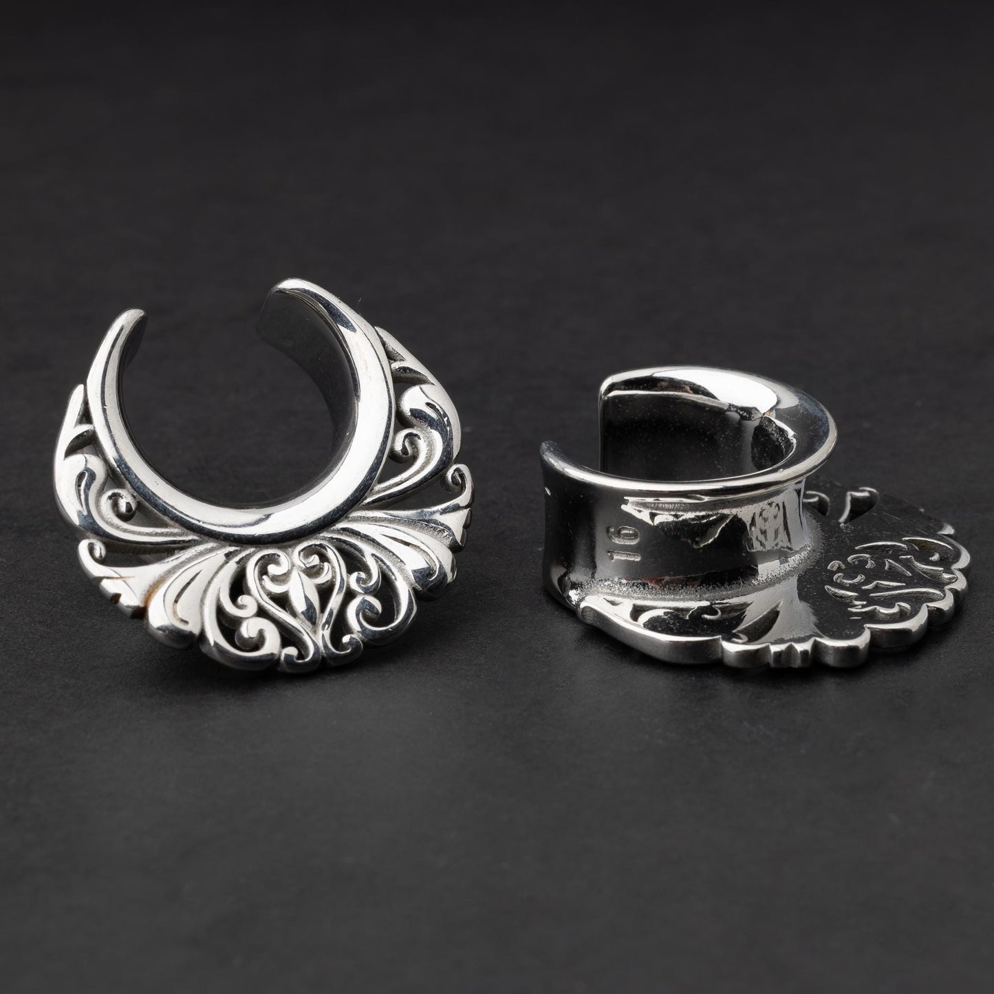 Pair of silver saddle tunnels with swirling decorative patterns for stretched ears.