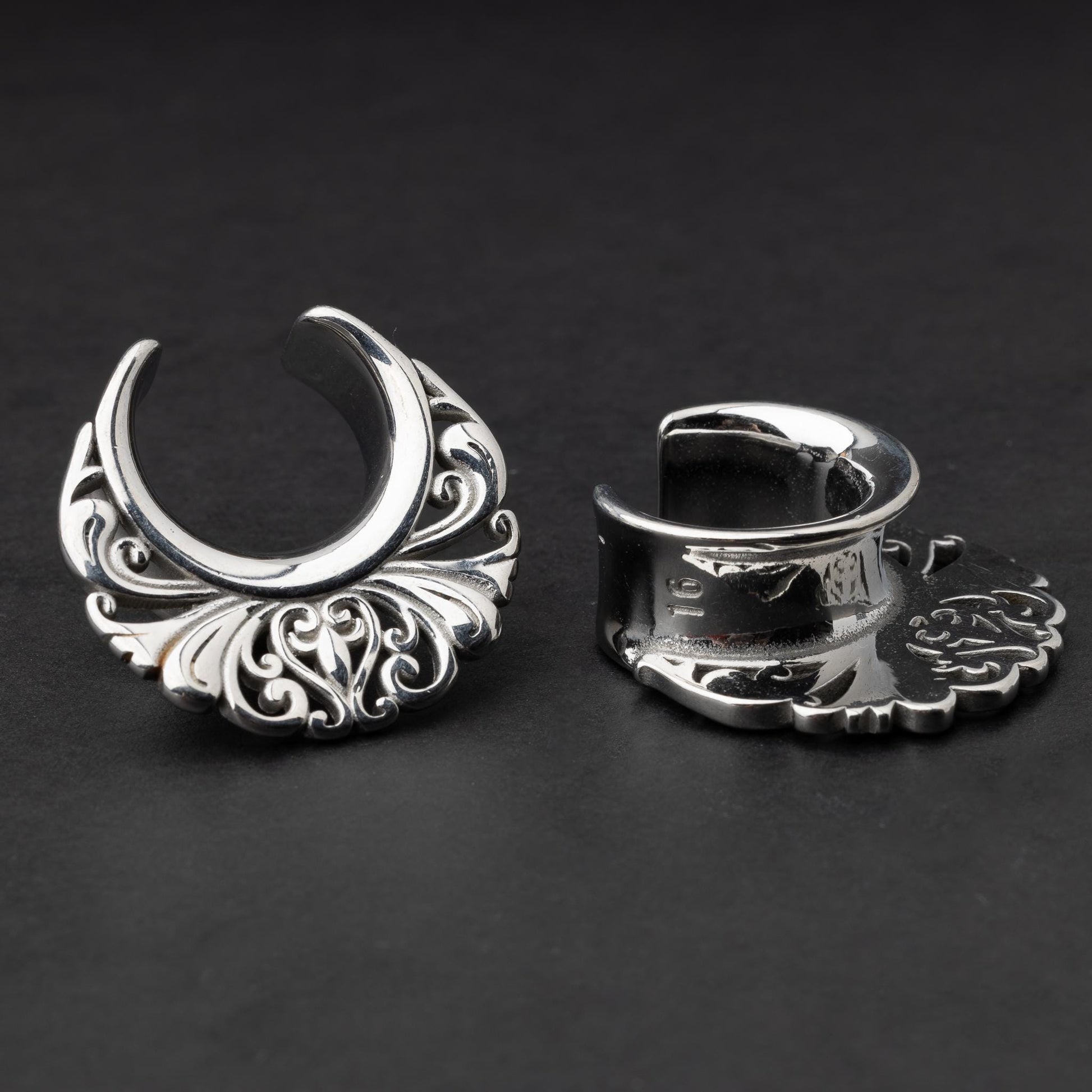 Pair of silver saddle tunnels with swirling decorative patterns for stretched ears.
