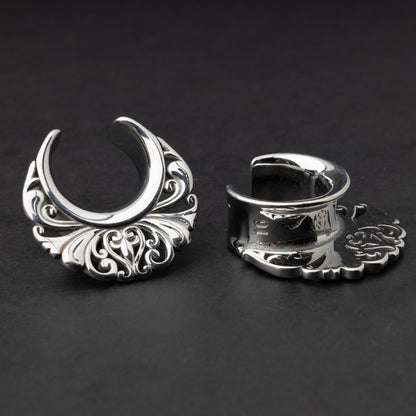 Pair of silver saddle tunnels with swirling decorative patterns for stretched ears.