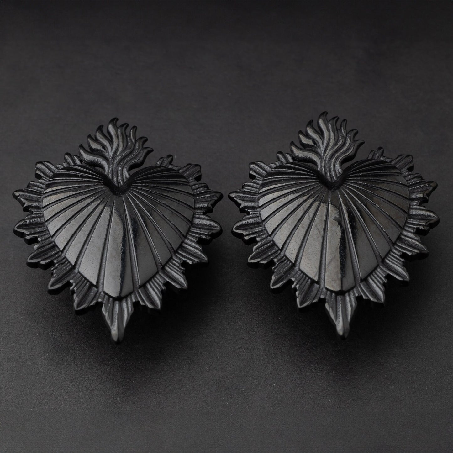 Sacred Heart-inspired plugs in black, displayed on a matte dark background, showcasing intricate detailing and a bold design.
