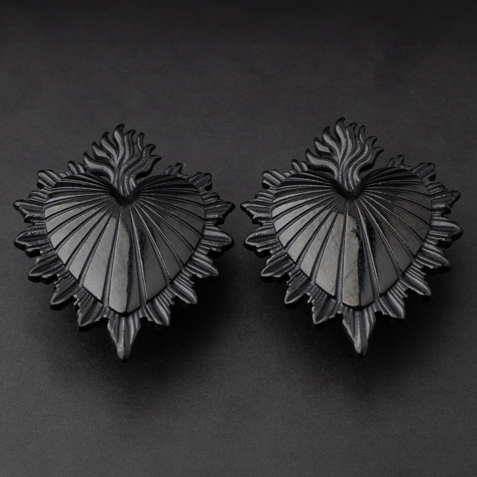 Sacred Heart-inspired plugs in black, displayed on a matte dark background, showcasing intricate detailing and a bold design.