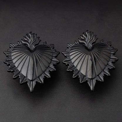 Sacred Heart-inspired plugs in black, displayed on a matte dark background, showcasing intricate detailing and a bold design.