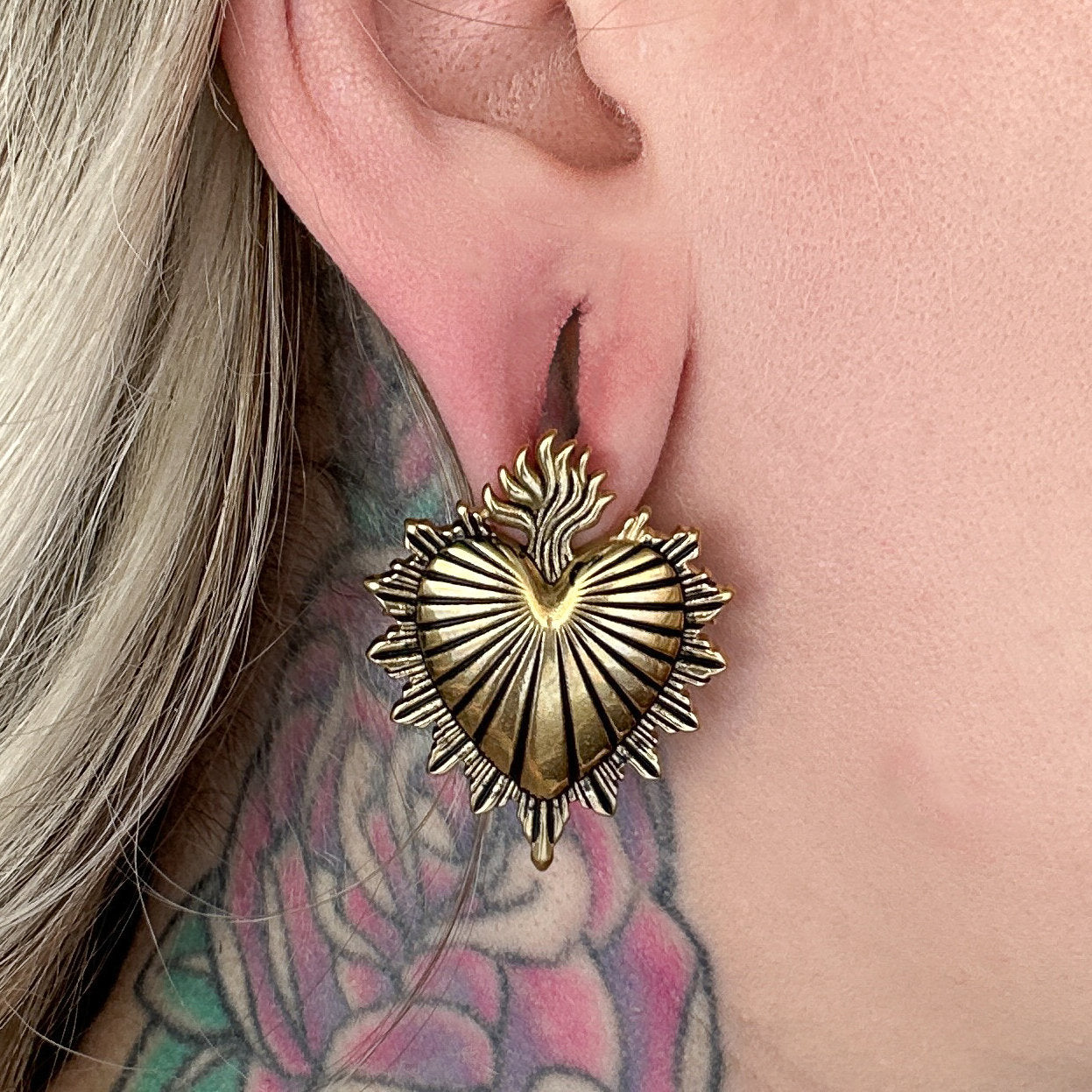 Three Sacred Heart-inspired plugs in black, silver, and gold tones, displayed on a models ear, showcasing intricate detailing and a bold design.