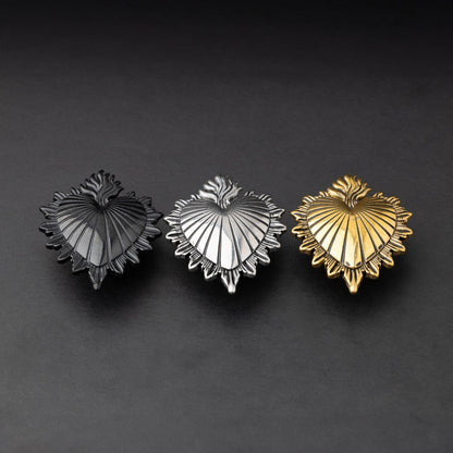 Three Sacred Heart-inspired plugs in black, silver, and gold tones, displayed on a matte dark background, showcasing intricate detailing and a bold design.