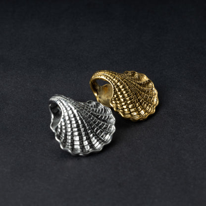 Two seashell-shaped ear weights, one in polished silver and one in polished gold, with detailed textures and a bold design, displayed on a dark background.

