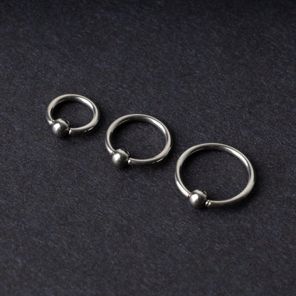 Three polished stainless steel captive bead rings of varying sizes displayed on a dark matte background.