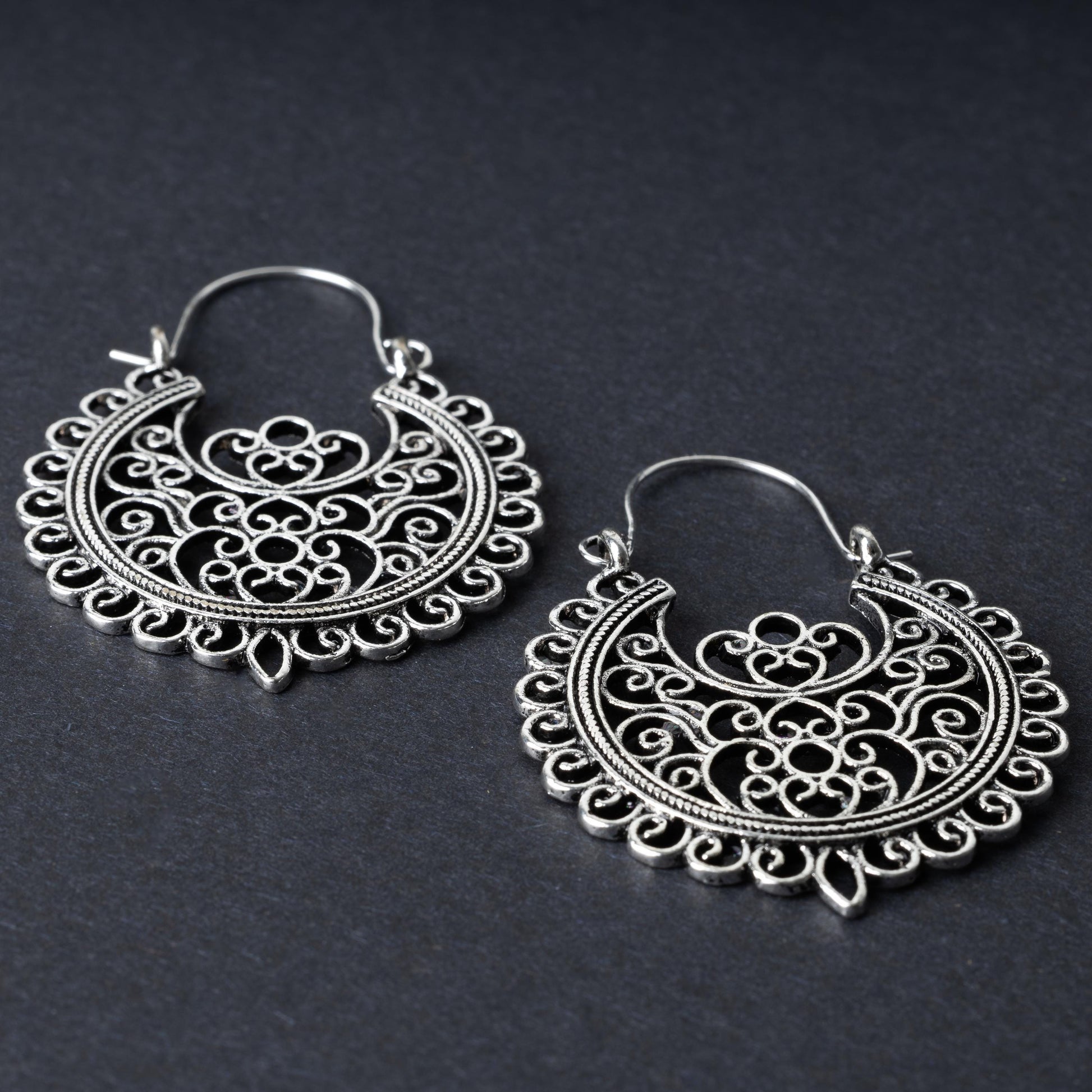 Pair of silver filigree hoop earrings with intricate scrollwork design, displayed on a dark background.