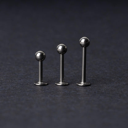Three silver stainless steel labret studs with flat backs and polished ball ends, displayed on a dark textured background.